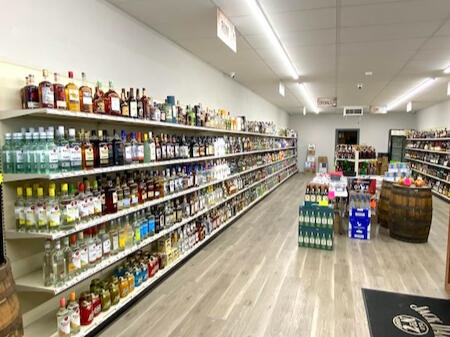 Gaslite Liquors – Extensive Premium Spirits & Wine Aisles A wide-angle interior view of Gaslite Liquors showing long, well-organized aisles of vodka, gin, rum, and cognac. The store features bright overhead lighting, clean wood-style flooring, and rustic wooden barrel displays near the checkout counter.
